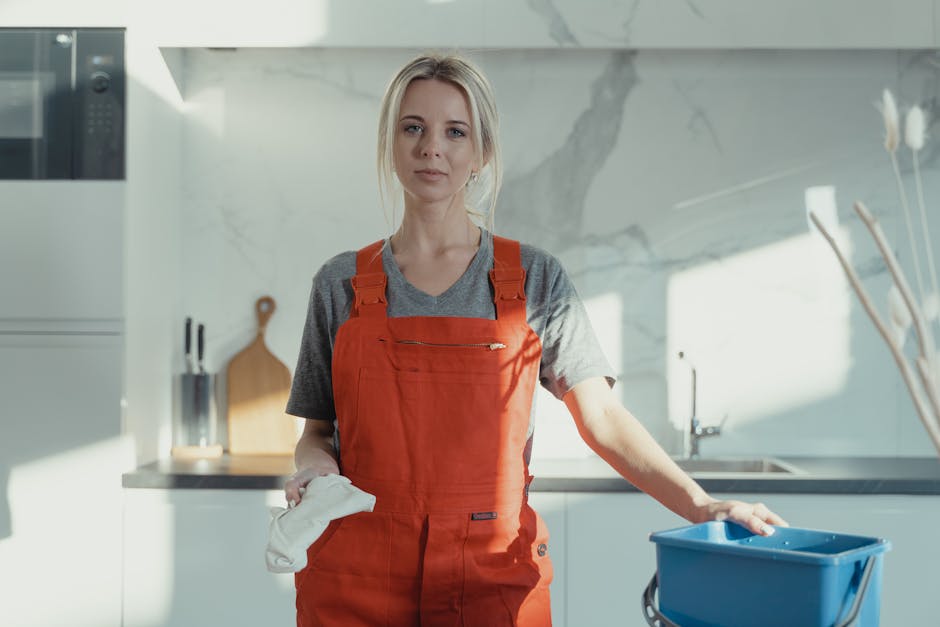 A black and white photo of three professional cleaners in a modern kitchen space, actively engaged in surface cleaning tasks. One woman stands near the left side holding a mop, with a bucket beside he